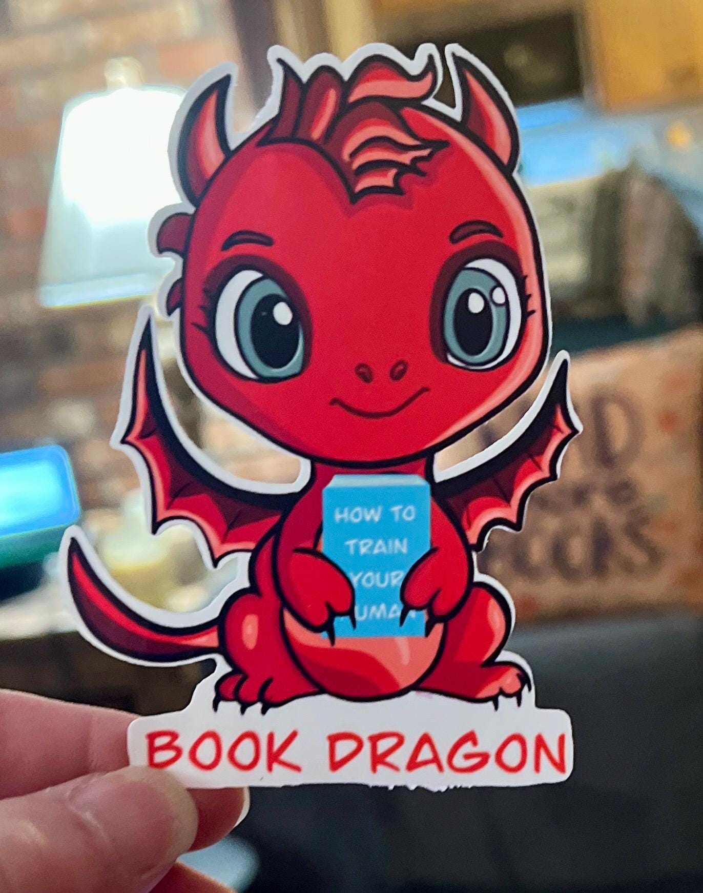Book Dragon Sticker | Cute Red Dragon Holding ‘How to Train Your Human’ Book | Waterproof Die Cut Sticker for Readers & Fantasy Lovers - Tomes and Troves