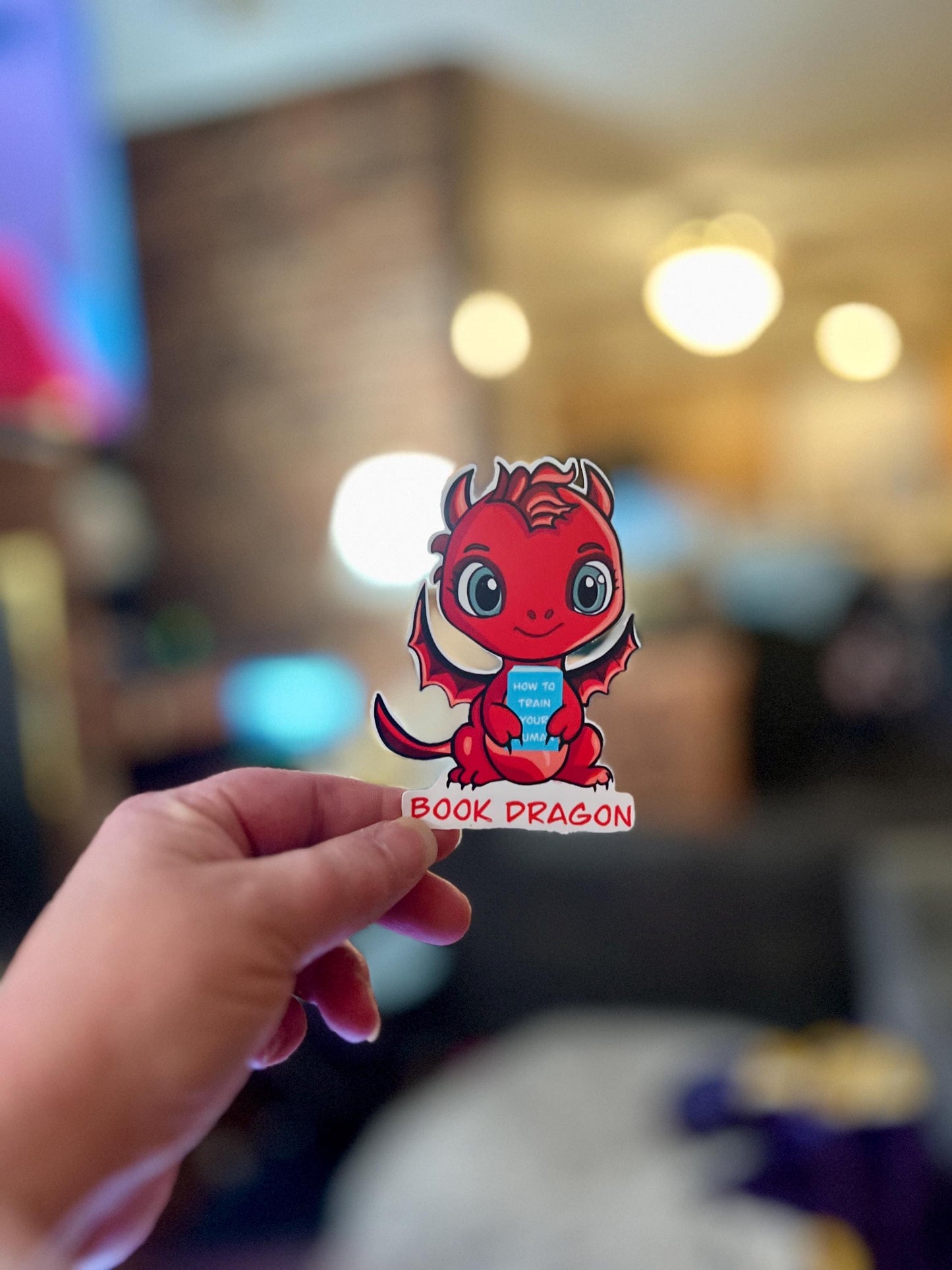Book Dragon Sticker | Cute Red Dragon Holding ‘How to Train Your Human’ Book | Waterproof Die Cut Sticker for Readers & Fantasy Lovers - Tomes and Troves